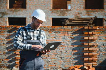 Engineer, bearded man wears safety helmet inspecting housing development project at construction...