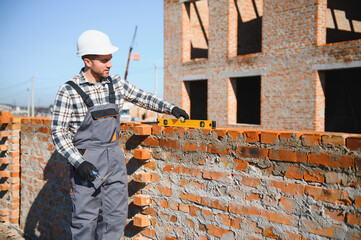 construction mason worker bricklayer installing red brick with trowel putty knife outdoors