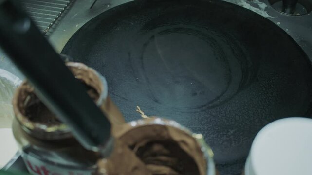 An overhead view of a clean, hot crepe griddle ready for use, surrounded by jars of chocolate spread and cooking utensils in a professional kitchen setup.