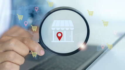 Hand holding magnifying glass focusing on local store icon with location pin, representing...