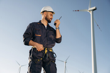 Communicating by walkie talkie. Engineer in field checking on wind turbine production