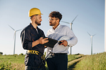 Making the business. Two men engineers are on field, with wind turbines
