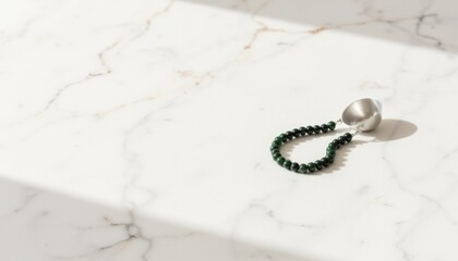 Elegant silver measuring spoon and green bead bracelet on marble surface illuminated by soft light