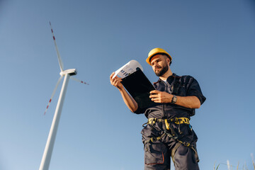 Documents in notepad. Engineer in field checking on wind turbine production