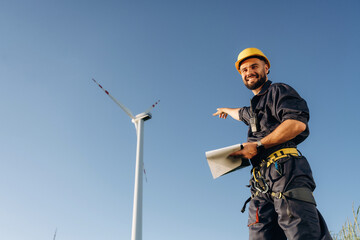 Pointing to the wind turbine by hand. Engineer in field on clean energy production