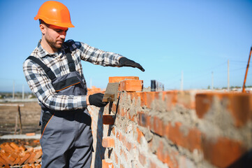construction mason worker bricklayer installing red brick with trowel putty knife outdoors