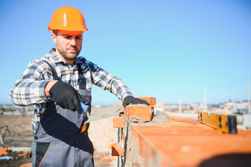 Male construction worker in uniform and helmet on construction of red brick house