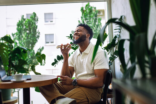 Smiling man sitting in coffee shop talking on phone via spiker.