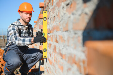 Male construction worker in uniform and helmet on construction of red brick house