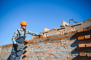 construction mason worker bricklayer installing red brick with trowel putty knife outdoors
