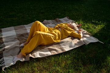 A serene scene of a woman dressed in yellow, leisurely relaxing on a blanket in nature, enjoying