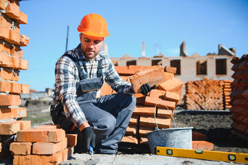 construction mason worker bricklayer installing red brick with trowel putty knife outdoors