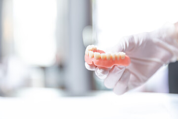 Upper denture held with gloved fingers in bright dental setting    © SWMedia