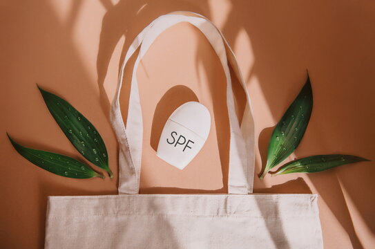 top view of eco bag with cosmetic product SPF cream and green leaves on orange background