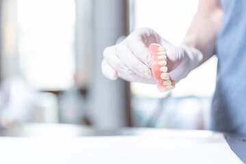 Dentist holding upper denture for elderly person in gloved hand    © SWMedia