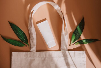 top view of eco bag with cosmetic product SPF cream and green leaves on orange background