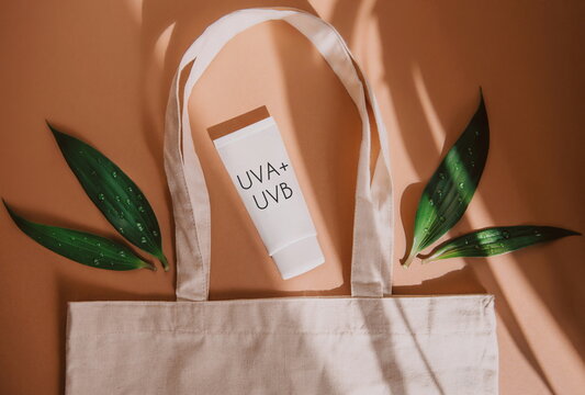 top view of eco bag with cosmetic product SPF cream and green leaves on orange background