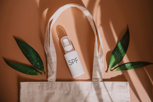 top view of eco bag with cosmetic product SPF cream and green leaves on orange background