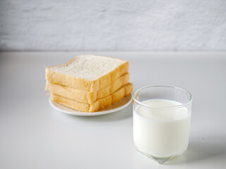 breakfast,Fresh milk in a glass and White sliced bread stacked on the white wooden table