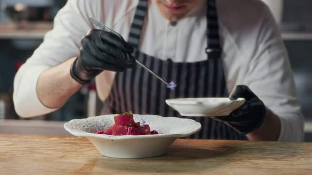 Zoom out shot of male chef garnishing tuna fillet cubes with edible flowers on plate before serving in fine dining restaurant