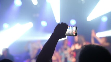 Concertgoers capturing live music performance, holding smartphones and recording band playing under bright stage lights, showcasing modern music experience and digital sharing culture