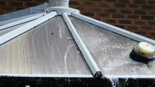 Cleaning bird dirt off a perspex roof of a sunroom using a power washer brush with soapy water
