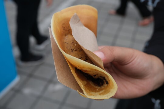 Crispy folded leker, a popular Indonesian street food, held by hand with paper wrapper, filled with chocolate and banana.