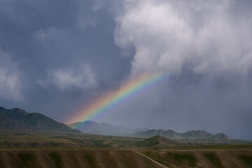 Rainbow in the mountains after a rain storm against a background of dark thunderclouds