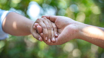 A close up of two people holding hands with a blurred background.