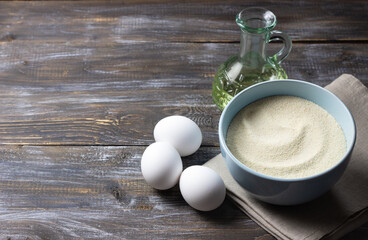 Semolina in bowl, eggs and vegetable oil on rustic wooden table, ingredients for homemade cooking and baking