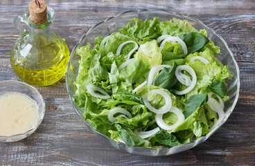 Fresh green salad with onion rings, olive oil and dressing on rustic wooden table, healthy organic meal top view