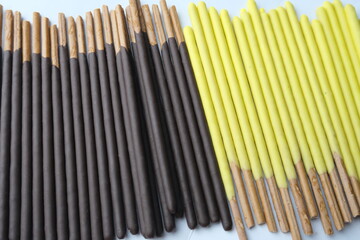 Side-by-side rows of biscuit sticks coated in dark chocolate and banana flavor, aligned on a white...