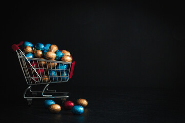 Basket with chocolate eggs in a shopping cart on a dark stone background.