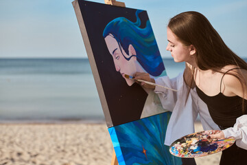 Young female artist paints vibrant canvas by seashore, capturing essence of creativity and...