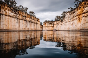 Calm river reflecting sandstone cliffs under a cloudy sky