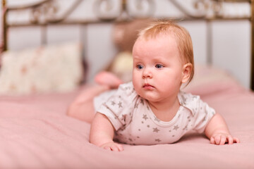 Infant female with light hair, fair skin, and blue eyes on pink bedspread. Star-patterned onesie...