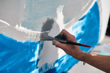 Close-up of adults hand painting abstract mural with brush. Blue and white are dominant. Scene is...