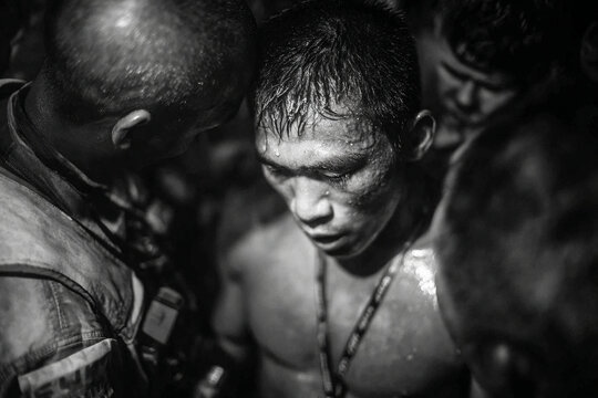 Focused muay thai fighter surrounded by his team in black and white intense moment showing sweat and determination