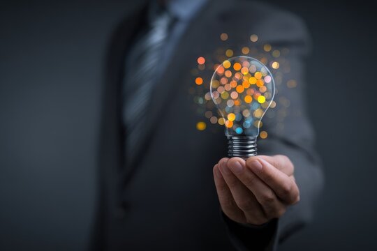 An elegant entrepreneur grasping a vibrant light bulb with glowing orbs against a dark backdrop