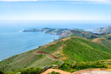 Scenic panoramic view of Marin Headlands with winding road, lush green hills, and Pacific Ocean coastline on a clear spring day, California nature landscape