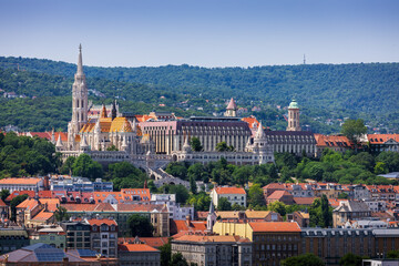 Panoramic view of Matthias Church and Fisherman's Bastion in Budapest, with Buda Hills in the background, captured from the dome of St. Stephen’s Basilica on a sunny summer day.