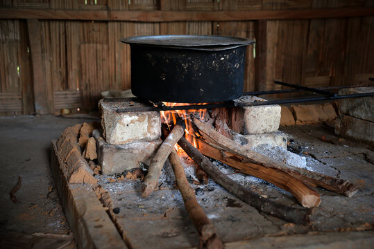 Cooking rice in a large pot over firewood inside a bamboo hut
