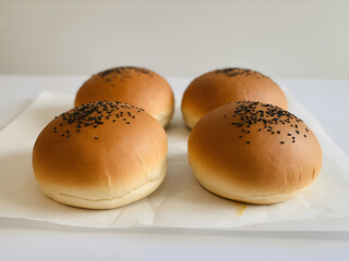 A close up shot of four burger buns with sesame seeds on a white surface in a well lit environment