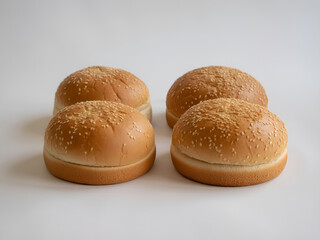 Four hamburger buns with sesame seeds on a white surface ready for making delicious sandwiches now