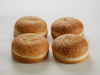 A close up shot of four sesame seed burger buns arranged on a plain white surface in a studio setting