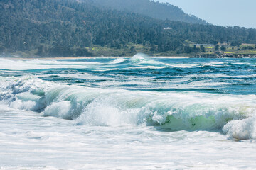 Powerful turquoise wave crashes onto the shore at Carmel River State Beach, California. A scenic view along the Pacific Coast capturing the raw beauty of the ocean and peaceful seaside landscape