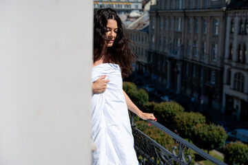 Young woman wrapped in white towel standing by window and balcony, enjoying quiet morning and soft...