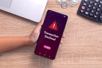 Hand holding smartphone with declined transaction notification on screen. Payment failed or...
