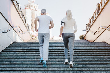 Rare back view of active senior couple in sportswear jogging together doing fitness exercises...