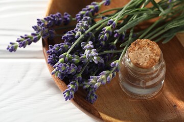 Natural essential oil and lavender flowers on white wooden table, above view